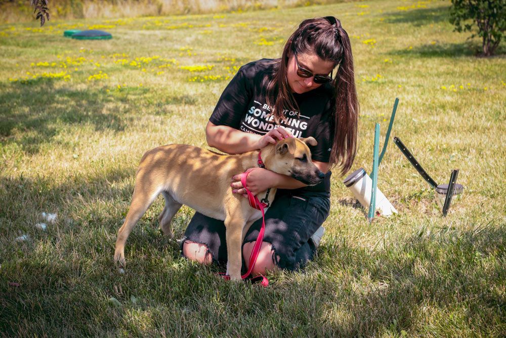 A woman kneels in the grass, playing with her dog