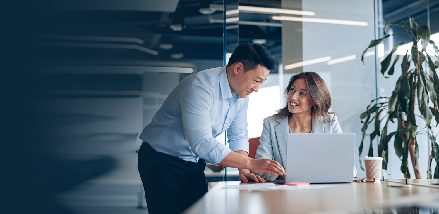 A man and woman discussing while focused on a laptop.