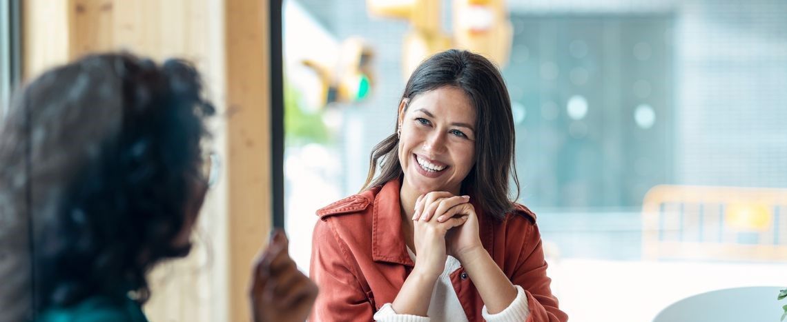 Two smiling women sit at a table, enjoying a friendly conversation