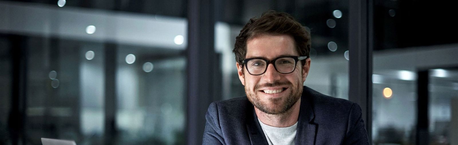 A cheerful man with glasses sits at a desk