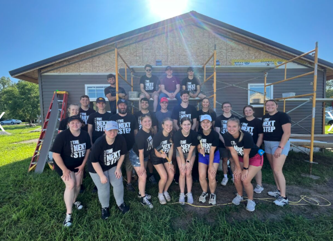 A group of young people in black shirts smiles together in front of a house