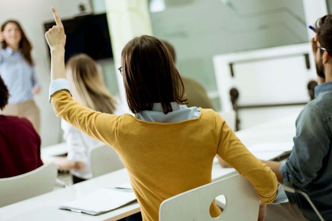 Woman in yellow raising her hand for a question in a business meeting